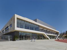 two people are walking in front of a large building with many windows on the outside