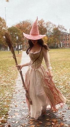 a woman dressed as a witch holding a broom and wearing a pink hat while walking down a path