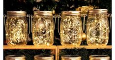 four mason jars with fairy lights in them on a shelf next to christmas tree branches