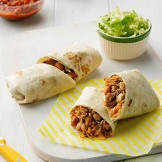 two burritos sitting on top of a cutting board next to a bowl of lettuce