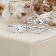 two wedding rings sitting on top of a white surface next to flowers and dried leaves