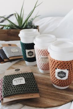 four coffee cups sitting on top of a wooden table next to a book and potted plant