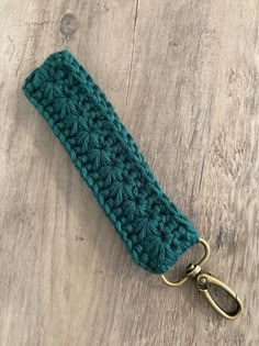 a green crocheted key fob on a wooden surface with a metal hook