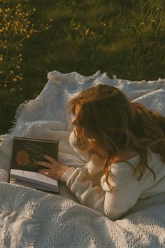 a young woman laying on top of a white blanket holding a book in her hands