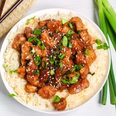 a white plate topped with meat and rice next to chopsticks on a table