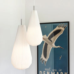 two white lamps hanging from the ceiling next to a poster with a bird on it