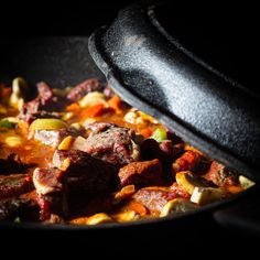 a skillet filled with meat and vegetables on top of a table next to a black pot