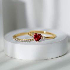 two gold rings with a heart shaped red stone and white diamonds on top of each other