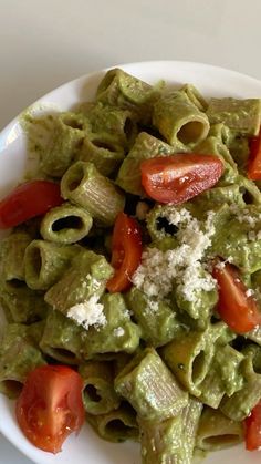 a white plate topped with pasta covered in pesto sauce and tomato slices on top