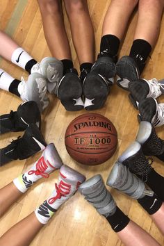 a group of people sitting around a basketball on top of a hard wood floor with their feet in the air