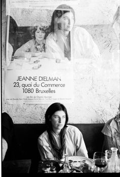 two women sitting at a table in front of a poster on the wall behind them