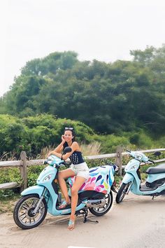 a woman sitting on top of a blue scooter next to a wooden fence