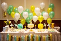 a table topped with lots of yellow and green balloons next to a cake covered in white frosting