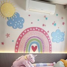 there are stuffed animals on the bed in this child's room with rainbow wallpaper