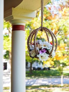 a flower arrangement hanging from a porch with a rope ring on the outside of it