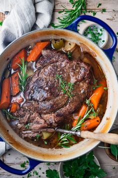 a pot filled with meat and vegetables on top of a wooden table next to carrots