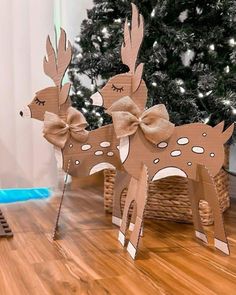 two wooden deer standing on top of a hard wood floor next to a christmas tree