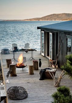 a deck with chairs and fire pit on the water's edge next to a house