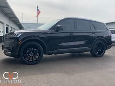 a black suv is parked in front of a building with an american flag on it