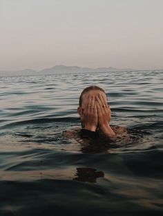 a person floating in the water covering their face with both hands and covering his eyes