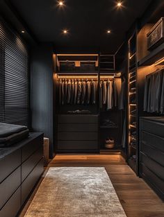 a walk - in closet with black walls and wooden flooring is lit by recessed lights