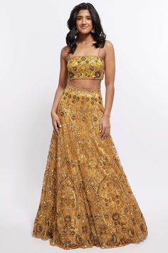 The Hasina Lehenga showcases intricate three-dimensional embroidery, comprising crystal, sequin, and beadwork in an ornate floral pattern adorning both the blouse and skirt. It is elegantly complemented by a matching skinny dupatta with beaded tassels. Designer Brocade Gold Dresses, Evening Gown With Zari Work For Festivals, Gold Brocade Dresses For Designer Wear, Gold Brocade Designer Dresses, Designer Gold Brocade Dresses, Glamorous Lehenga For Reception, Hand Embellished Party Wear Sharara For Reception, Fitted Tissue Silk Embroidered Fabric For Designer Wear, Bollywood Style Dress With Gold Embroidery For Reception