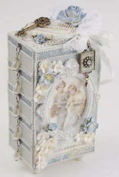 a small box with an angel on it and flowers around the edges is decorated with pearls