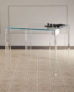 an acrylic table with clear legs and a glass top in front of a white wall