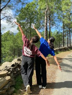 two people standing on the side of a road pointing at something in the air with their hands up