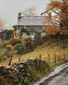 an old stone house sitting on the side of a hill next to a tree filled hillside