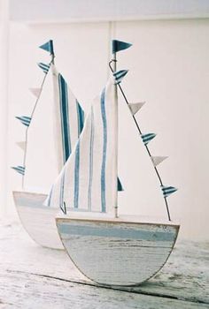 a small sailboat with blue and white sails on a wooden table in front of a wall