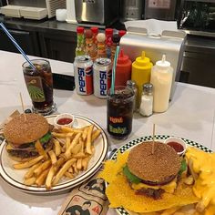 two plates with hamburgers and fries on them sitting on a table next to soda bottles