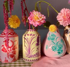 three vases with flowers painted on them sitting on a table cloth next to each other