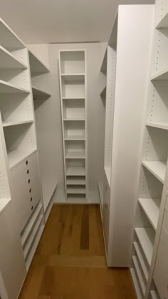 an empty walk in closet with white shelving and wood flooring on the side