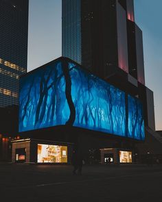 a large billboard is lit up in front of some tall buildings at night with people walking around