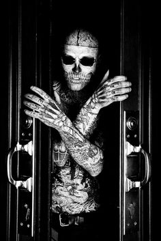 a man with tattoos and piercings standing in front of a door holding his hands out