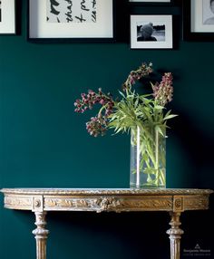 a vase filled with flowers sitting on top of a wooden table next to framed pictures