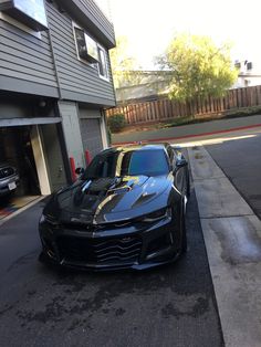 a black sports car parked in front of a garage on the side of a road