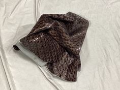 a brown snake skin bag sitting on top of a white sheet covered in plastic wrap