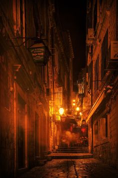 an empty street at night with lights on and no cars parked in the alleyway