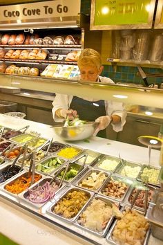 a woman standing in front of a counter filled with lots of different types of food