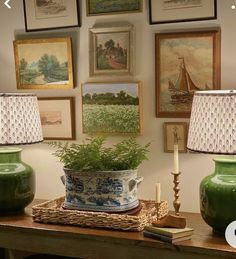 two green vases sitting on top of a wooden table next to lamps and pictures