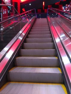 an escalator with red lights going up and down the stairs in a building