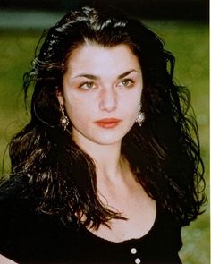 a woman with long black hair and earrings posing for a photo in front of some grass