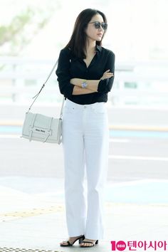 a woman in black shirt and white pants with her arms crossed standing next to a wall