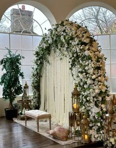 a wedding ceremony setup with white flowers and greenery on the wall, surrounded by two arched windows