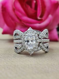 an oval cut diamond ring sits next to a pink rose