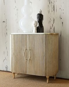 a white vase sitting on top of a wooden cabinet next to a black statue and lamp