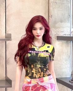 a woman with long red hair standing in front of a wall wearing a t - shirt and skirt