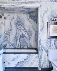 a bathroom with marbled walls and flooring, including a bathtub in the corner